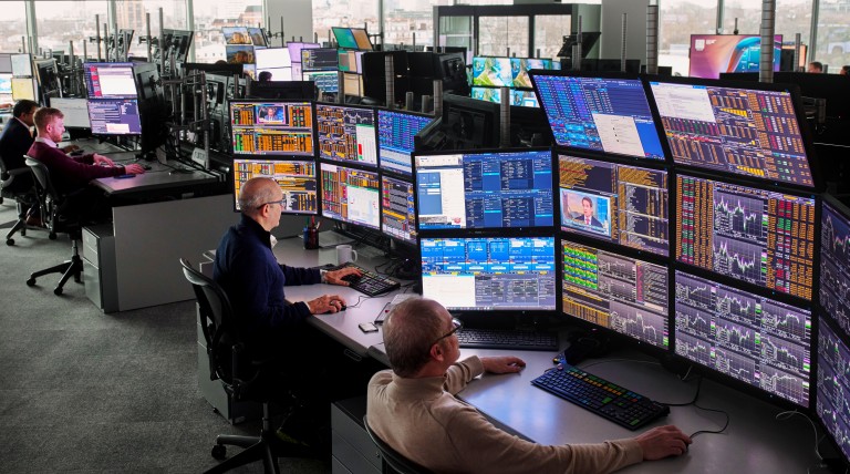 Trading floor with multiple screens displaying market analyses and price data, employees monitoring energy information with a view of the city skyline.